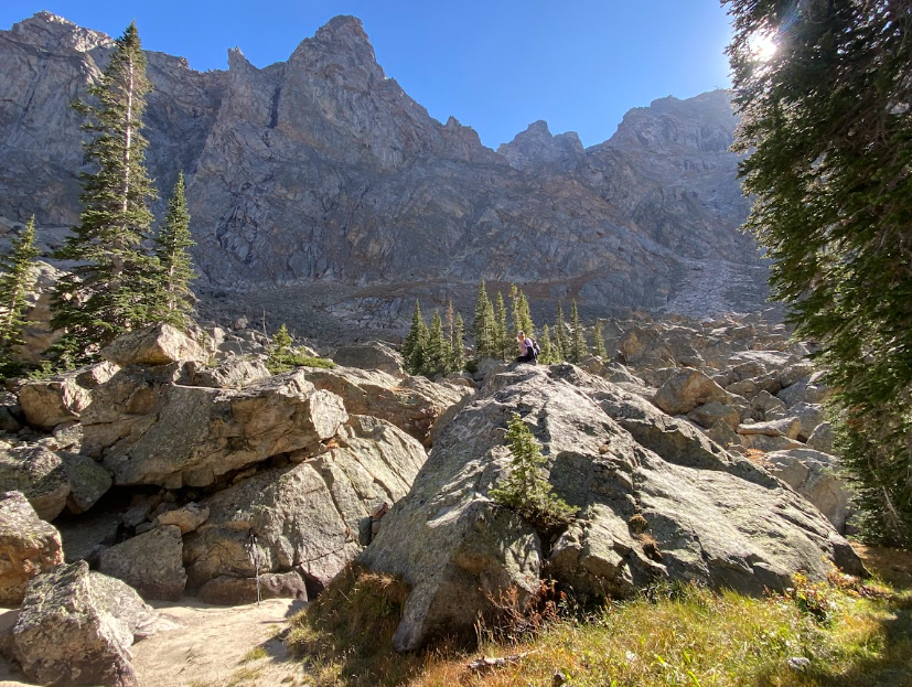 hiker poses on massive boulder while another hiker takes her picture and mountains loom in the short distance