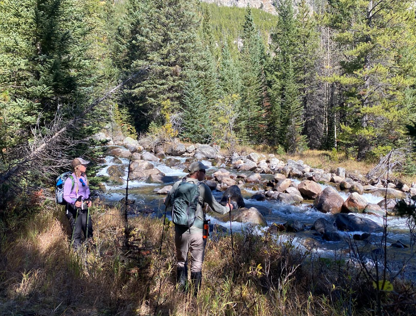 two hikers look into a creek full of big boulders