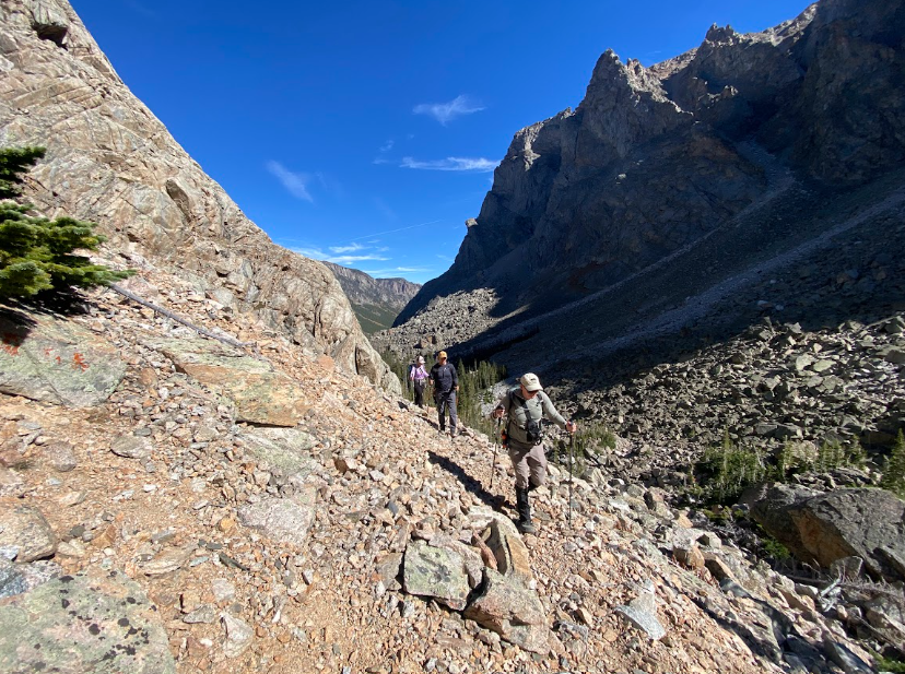 three hikers walk through a scree field on the side of canyon wall