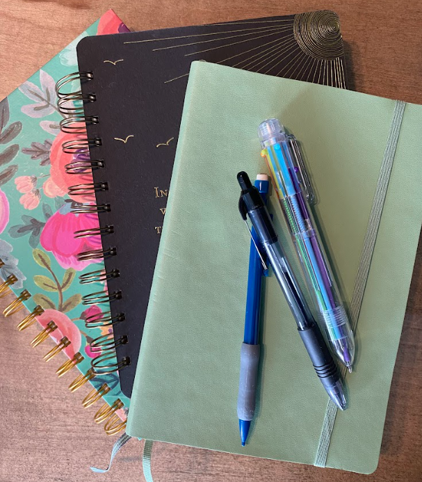 stack of colorful journals with pens and pencils
