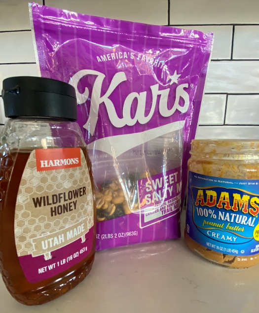 from left to right a squeeze bottle of honey, Kar's brand of sweet and salty trail mix, and a jar of Adams 100% natural peanut butter