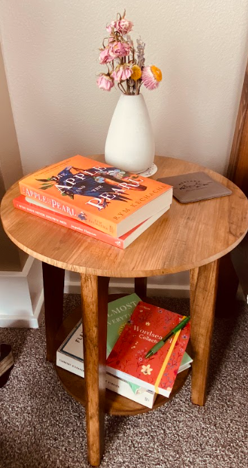 small round bedside table with books on top along with a vase of dried flowers and a stack of books below