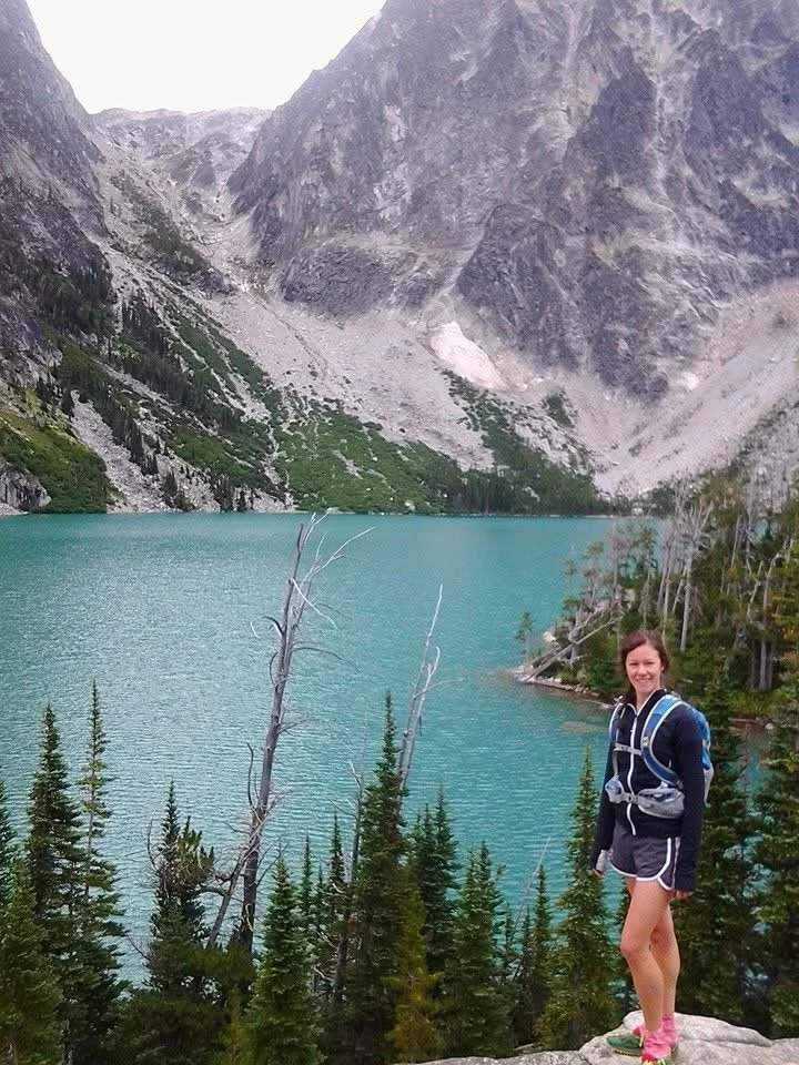 Sprite poses in front of a cerulean blue lake with granite mountain backdrop