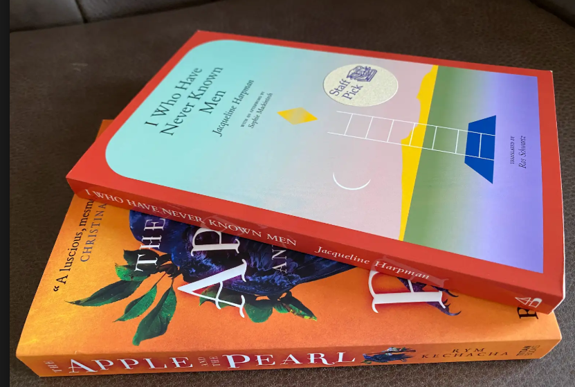 two stacked books; The Apple and the Pearl with orange cover and dark image in center then, top book I Who Have Never Known Men edged in red and cover in light blue with a ladder in the center