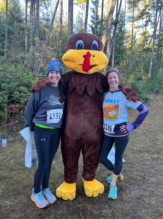 two runners pose on either side of a person dressed in turkey costume