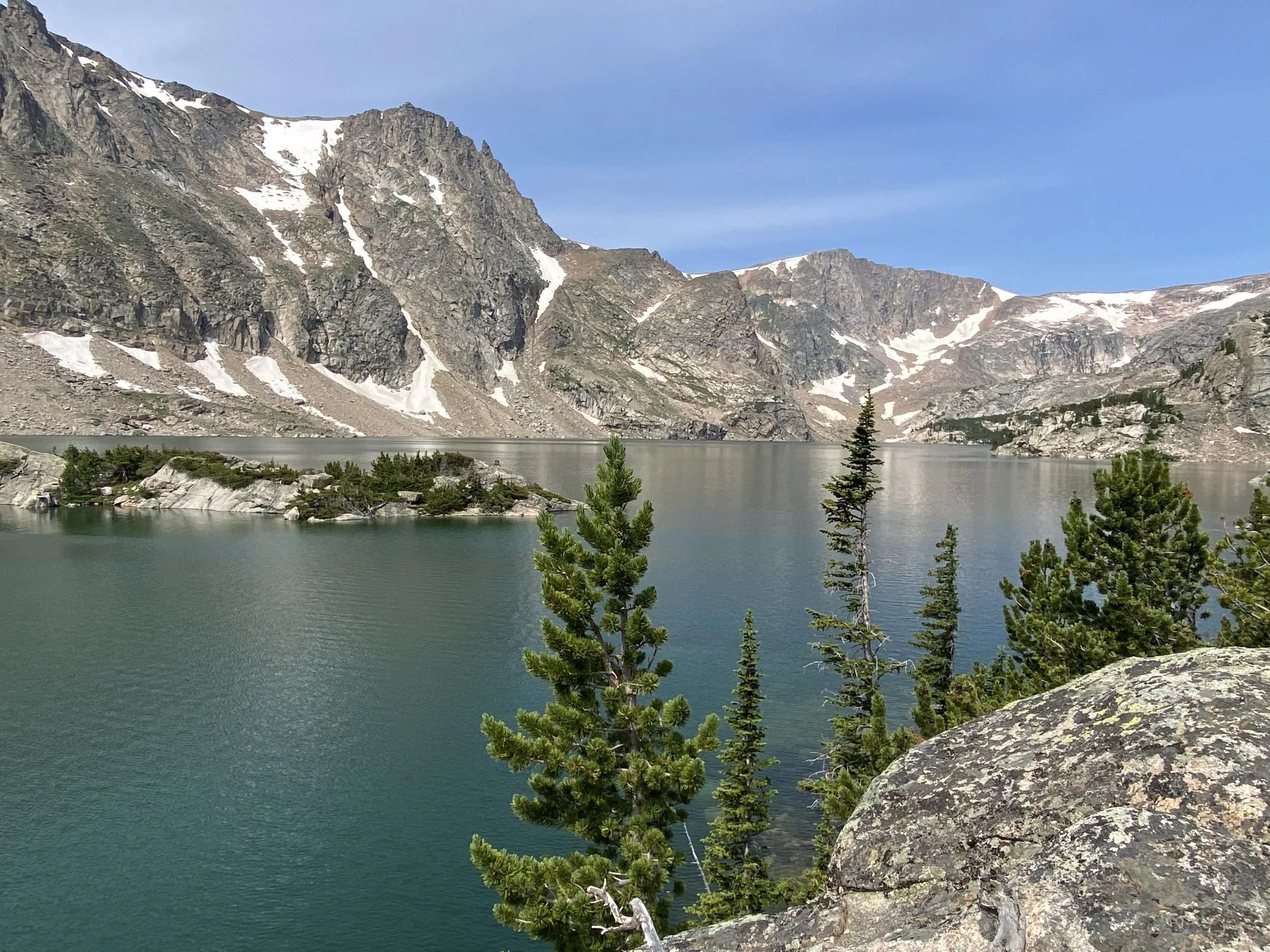 a placid blue lake with a shoreline of granite mountain walls that contain snowy patches