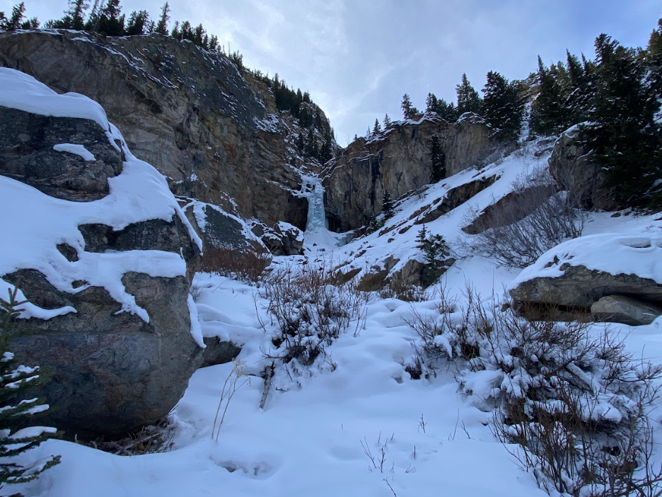 snow leading upwards to a tan rock wall with a frozen waterfall in the middle