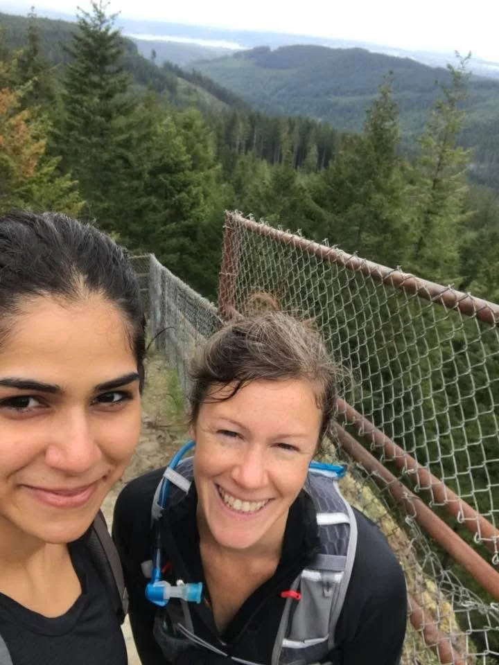 southeast Asian woman and white woman smile for selfie with pine trees and rolling hills as backdrop