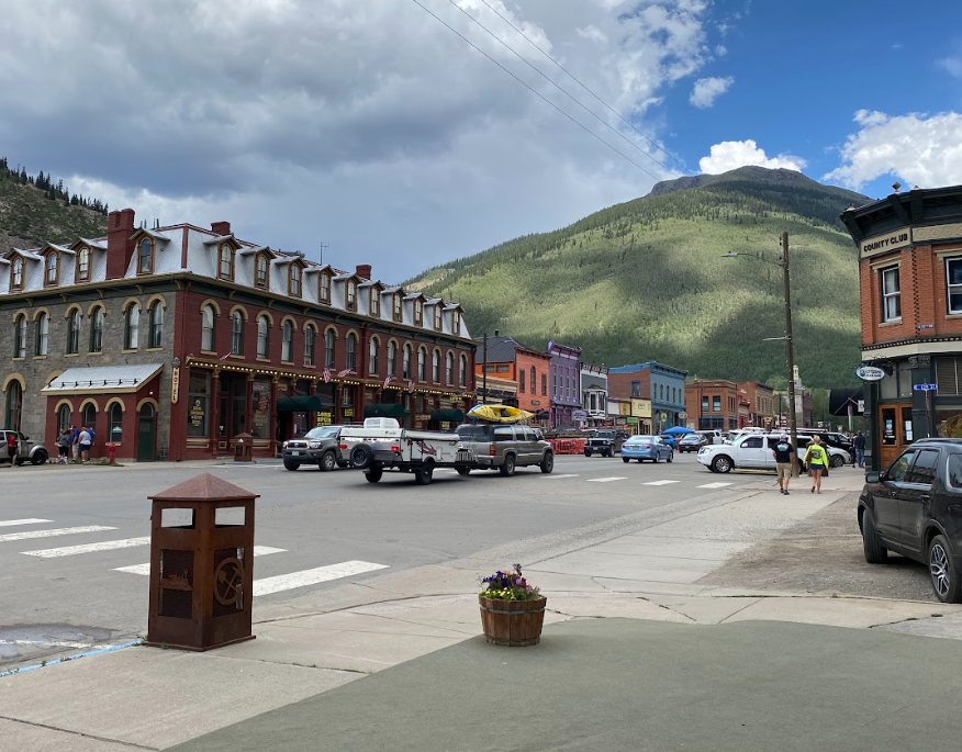 a busy scene in an old west town with colorful buildings and a green mountain just past the end of the street