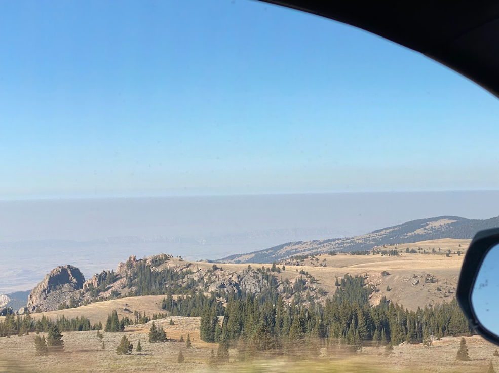 dry grass and evergreens lead into a rock outcropping under a hazy blue sky