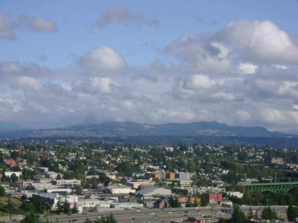 a sprawling city view with hillsides in the background under dense puffy clouds