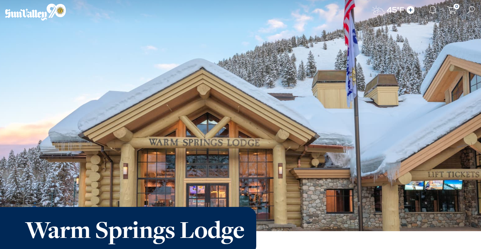 tan lodge made of logs has a roof of snow and a flag pole by its entrance