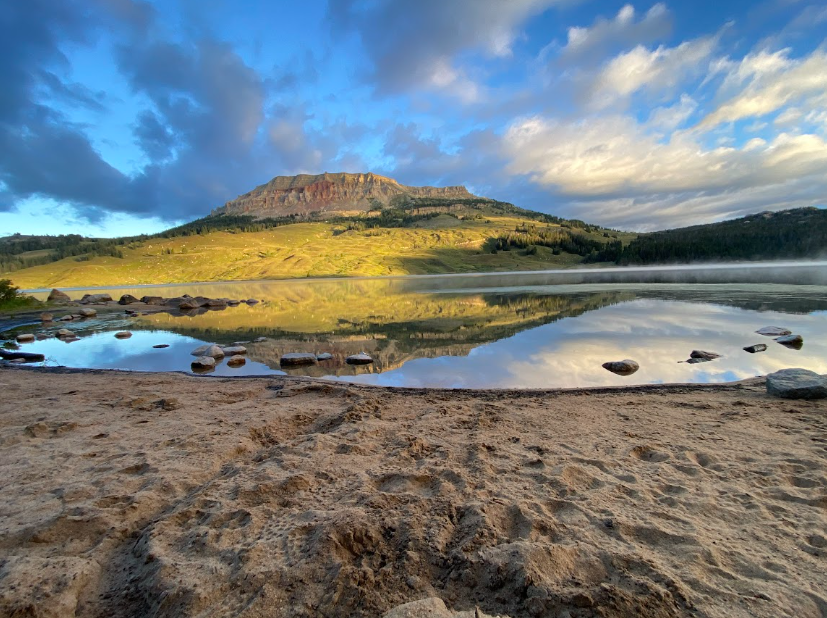 from a sandy shore by a lake the picture focuses on a bright green hillside below a limestone outcropping shaped like a molar from the back of your mouth