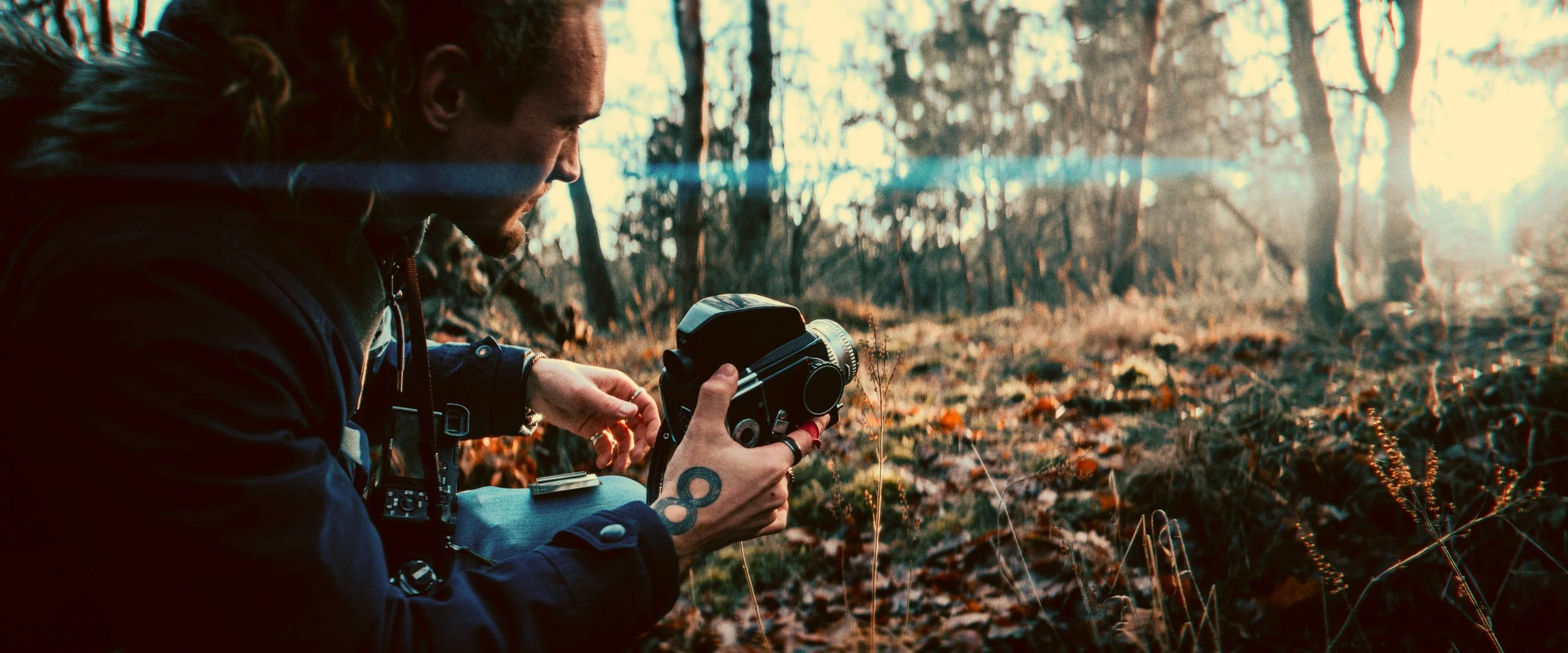Person outdoors holding a vintage camera, surrounded by forest foliage and sunlight filtering through the trees.