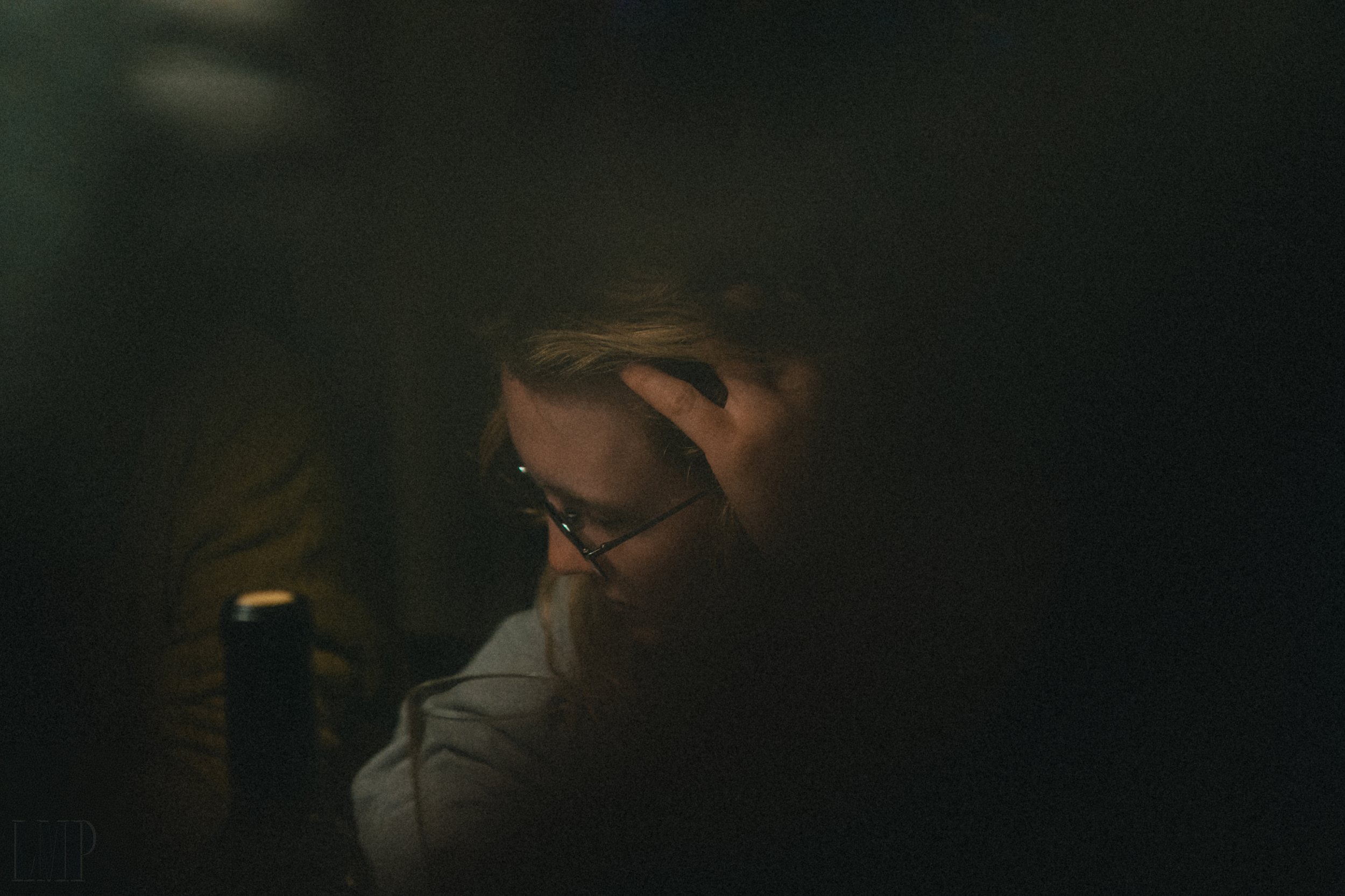 Dimly lit image of a person with glasses looking down, partially obstructed by shadows and darkness.