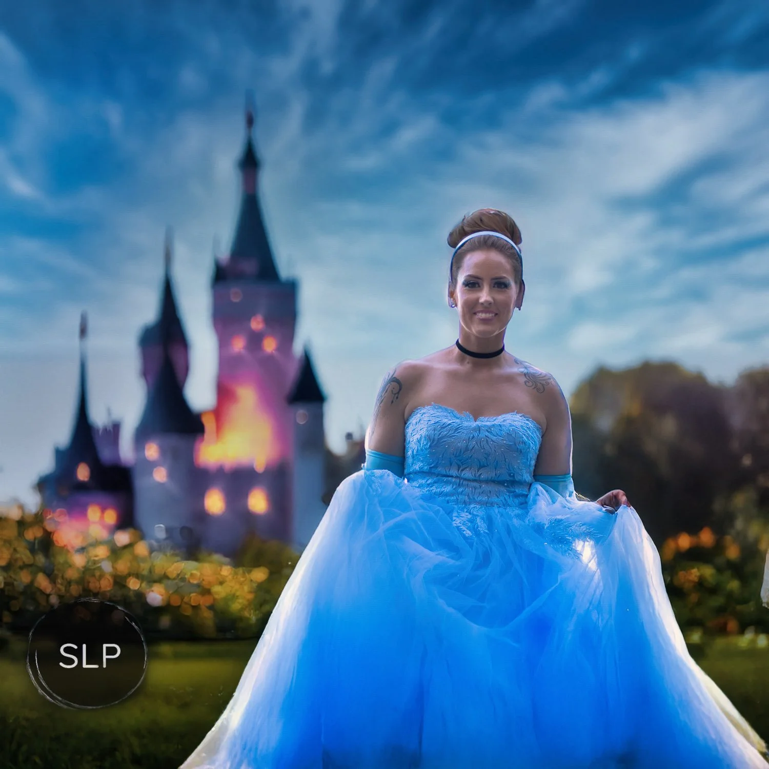 A young woman in a blue princess dress standing outdoors with a castle in the background during twilight.