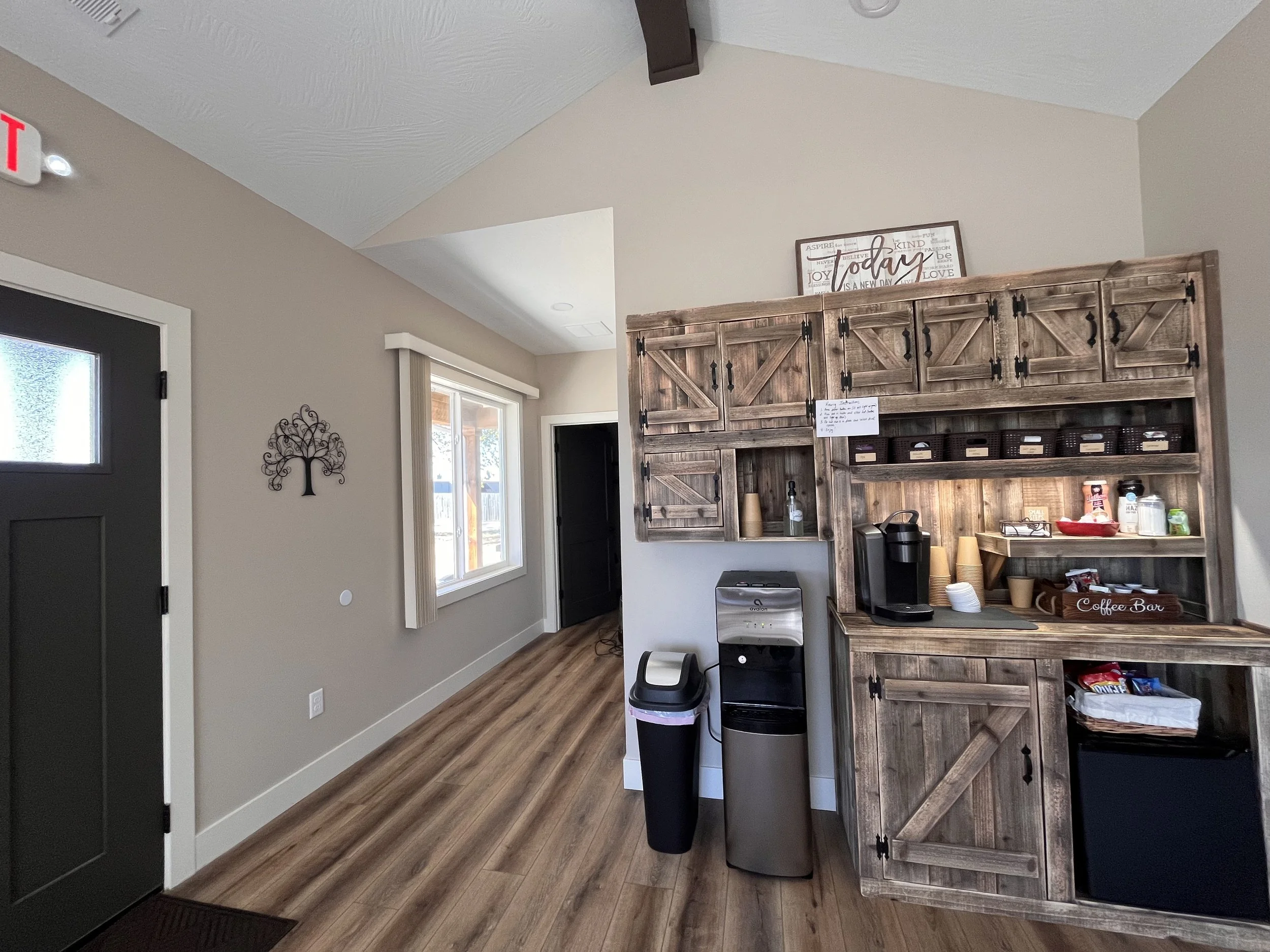 All Things New Counseling snack and beverage station with wooden cabinets, coffee machine, cups, and snacks in a cozy kitchen corner.