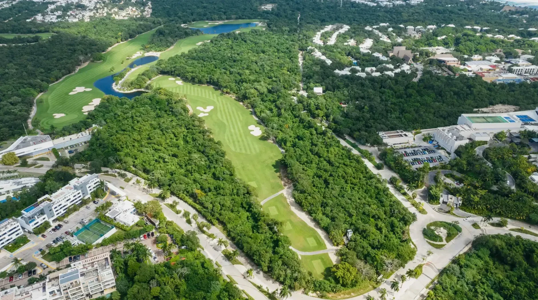 An aerial view of El Coyote golf course at Corasol winding through dense trees, with a few buildings and tennis courts visible on the outskirts.