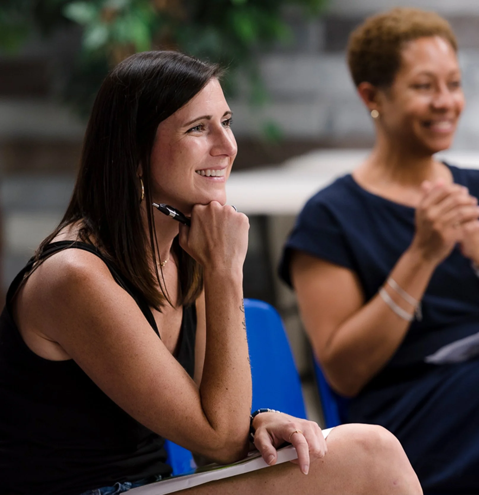 Two women sitting and smiling, one holding a pen and notepad, enjoying the reformed teaching at Old Cutler Presbyterian Church where Christ-centered, biblical teaching is the focus.