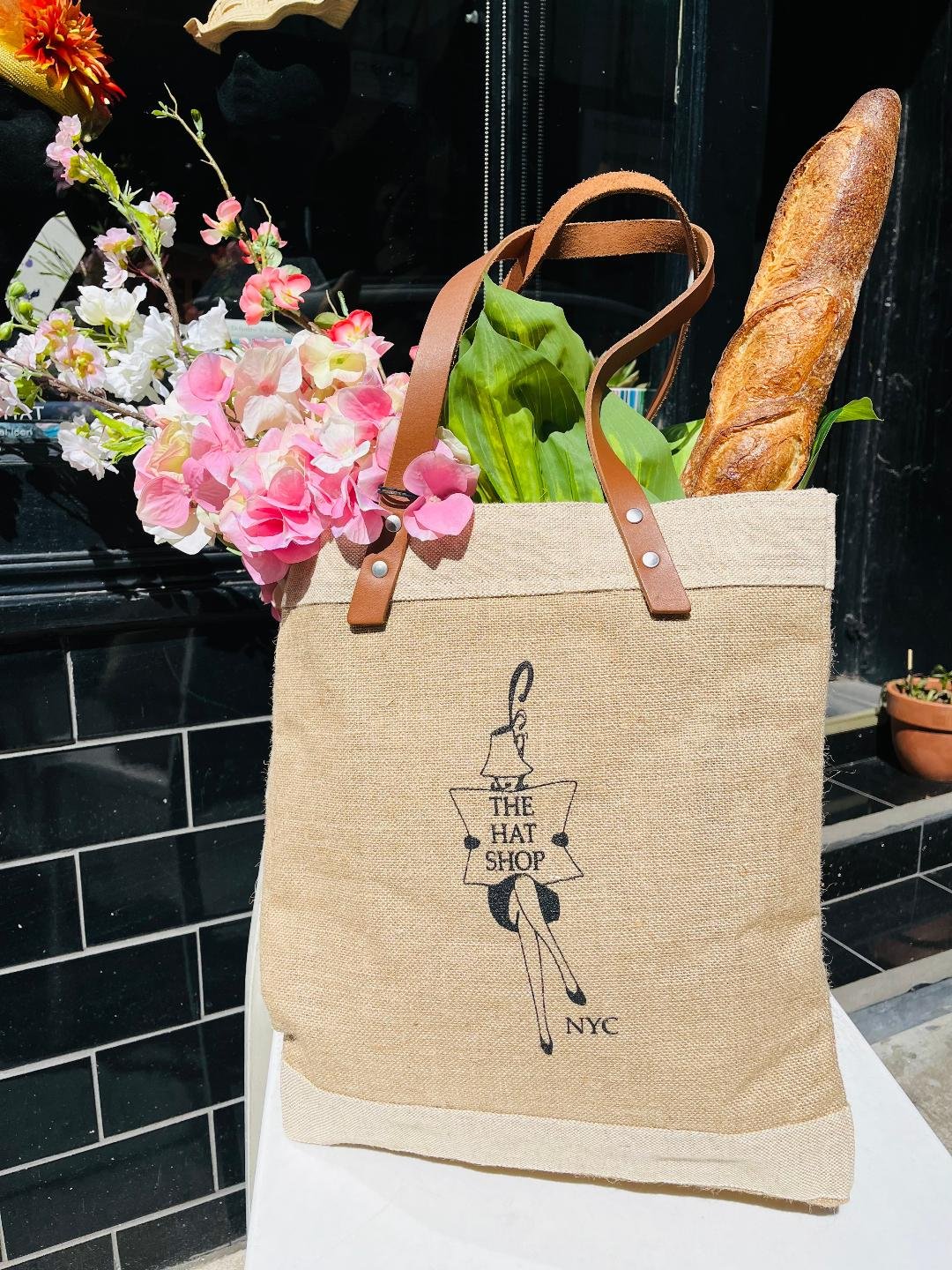 The Hat Shop Market Bag front view. The tote bag is filled with flowers and is outside The Hat Shop storefront.
