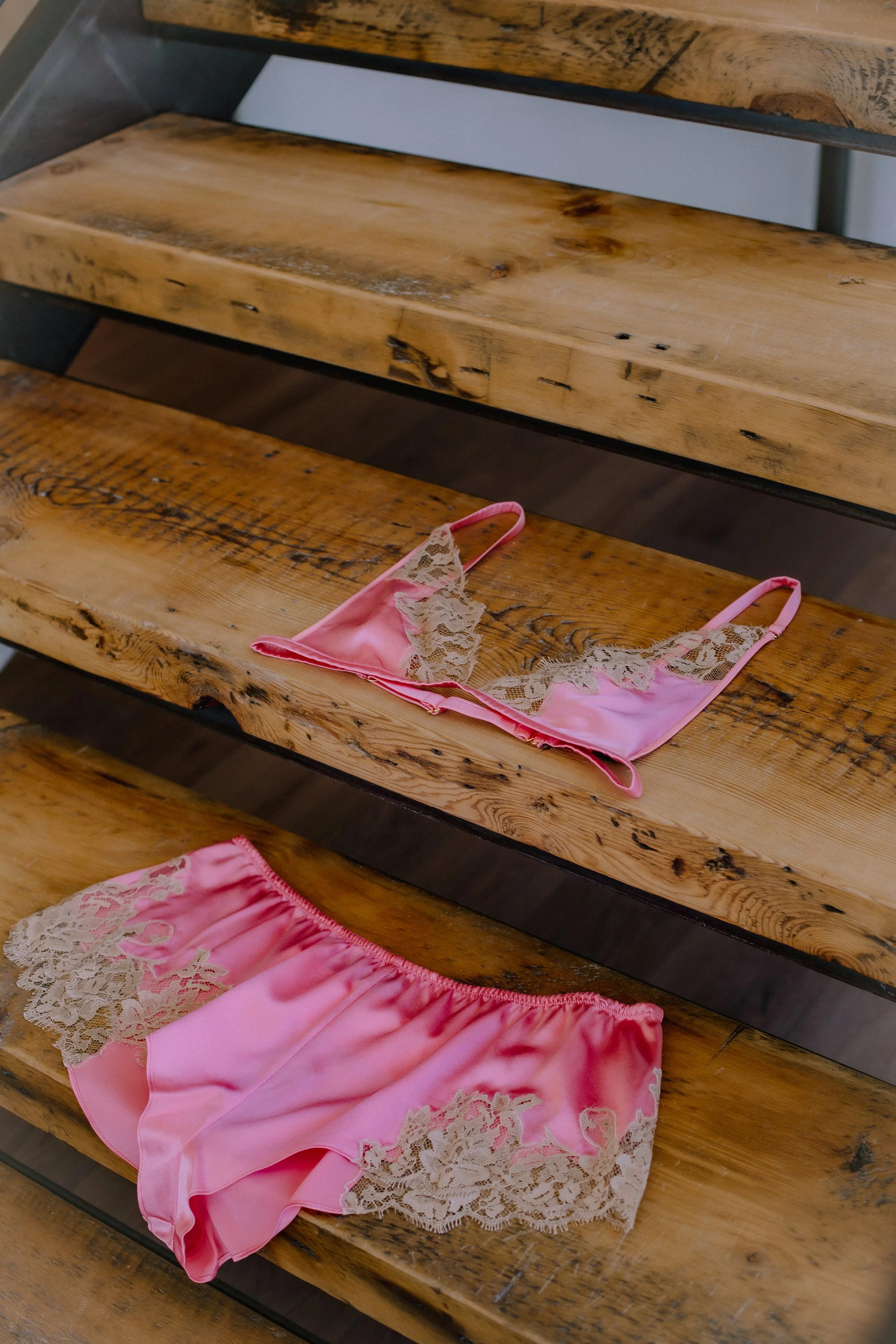 Pink silk lingerie with lace details placed on wooden steps.
