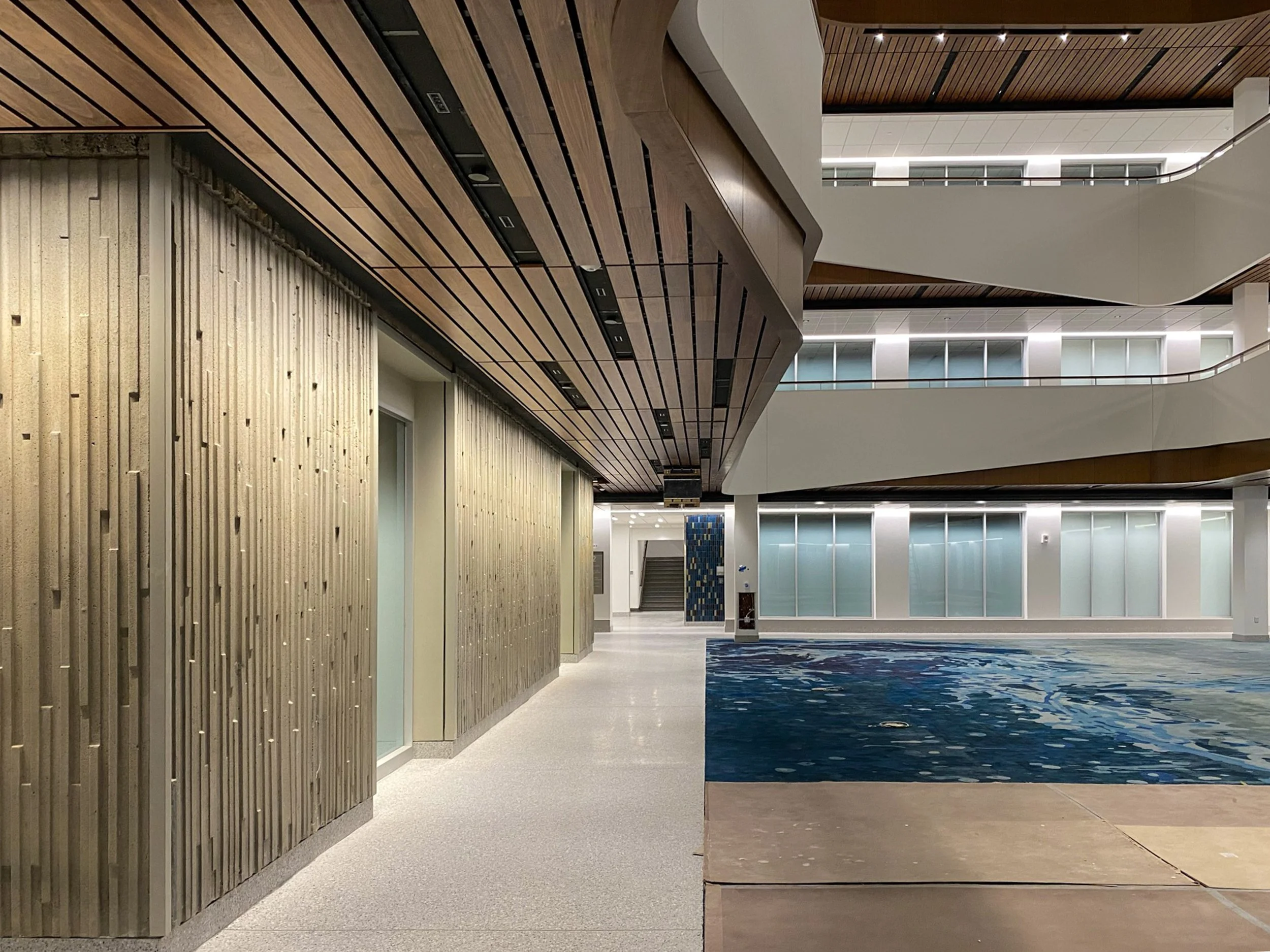 University lab building atrium lighting design with concealed lighting throughout, including grazing light on textured precast concrete walls, uplighting into the skylight well, and louvered downlights.