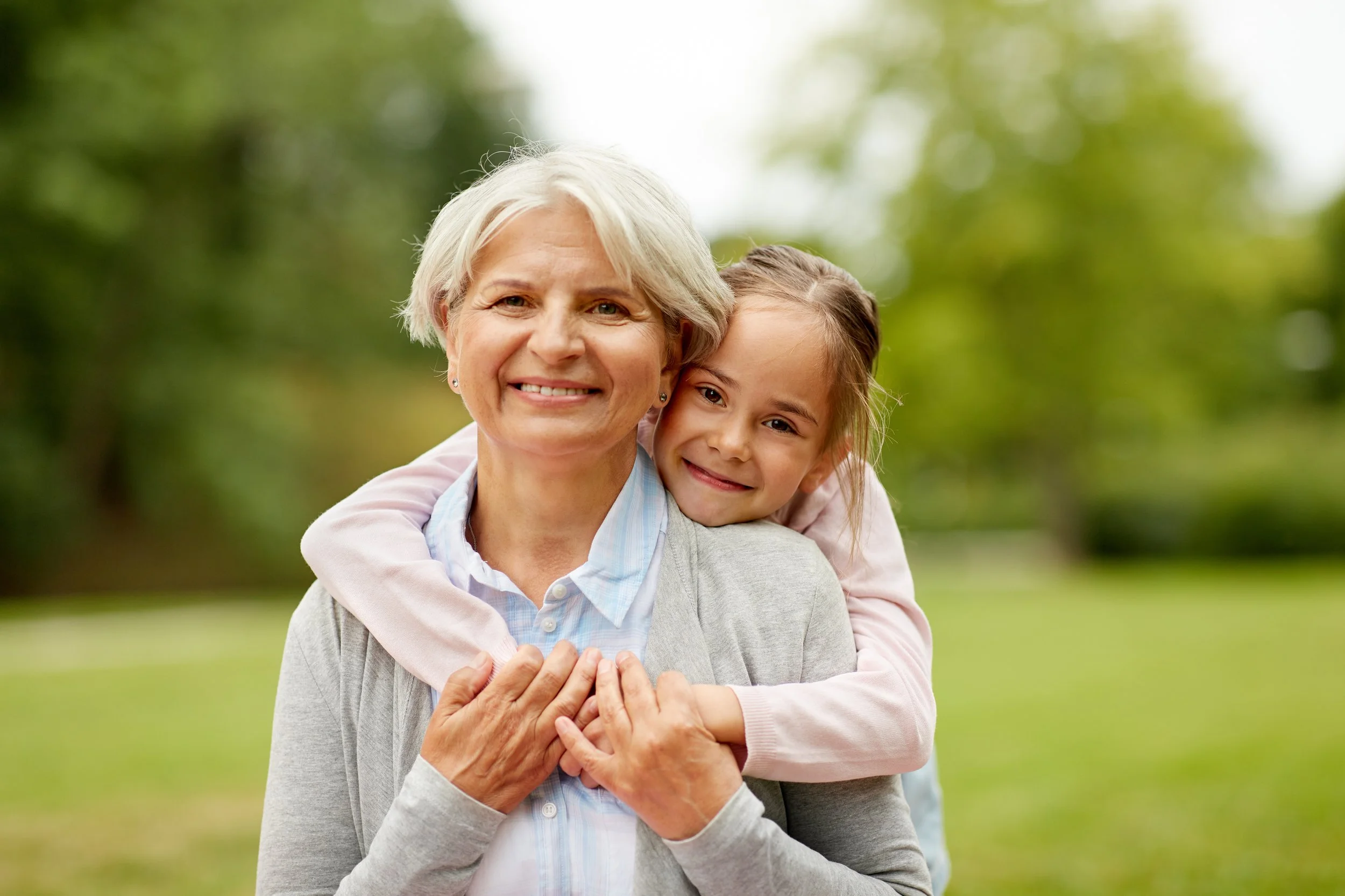 grandmother-hugging-granddaughter-both-smiling-outside