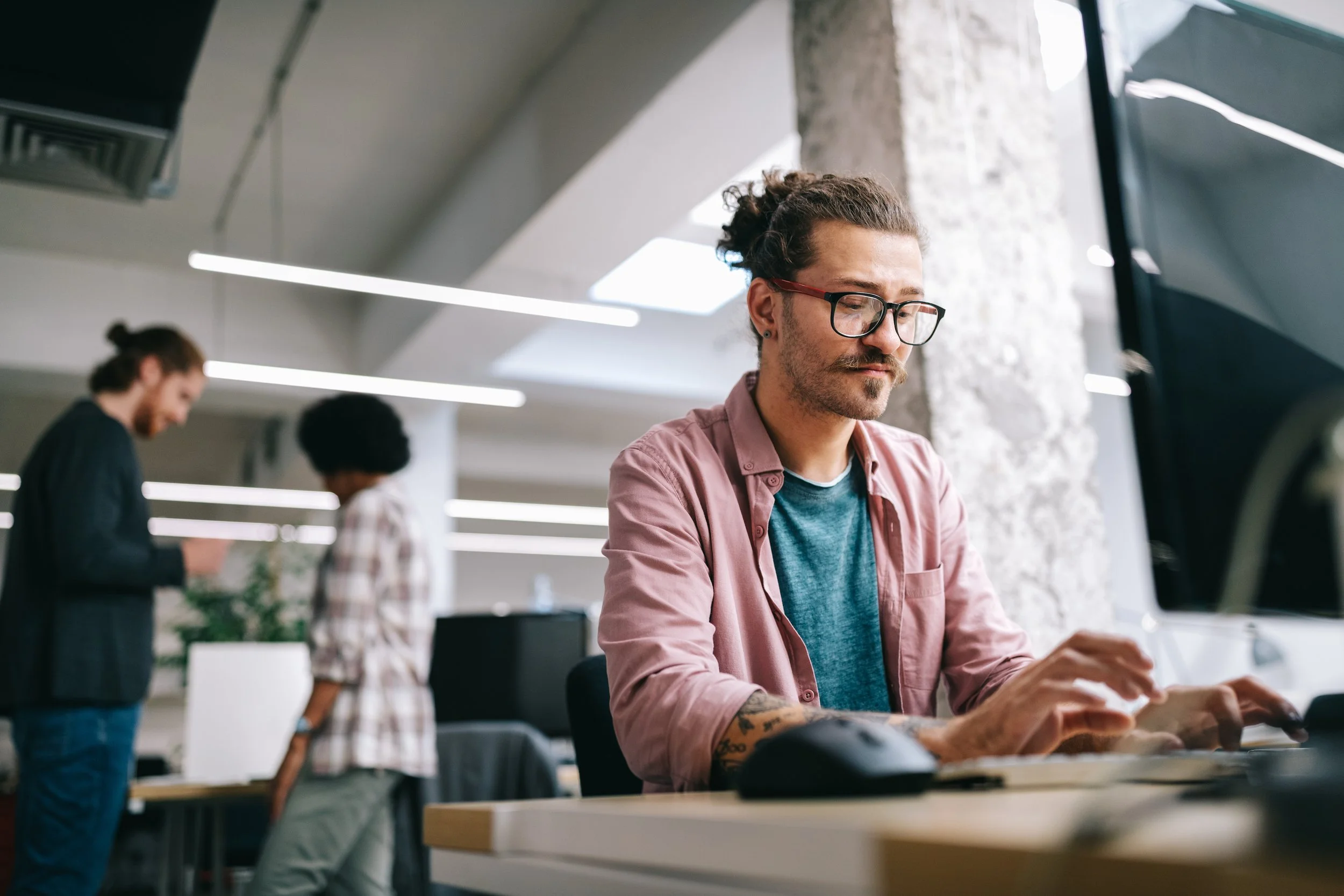 man-with-glasses-at-desk-in-office-typing-at-computer