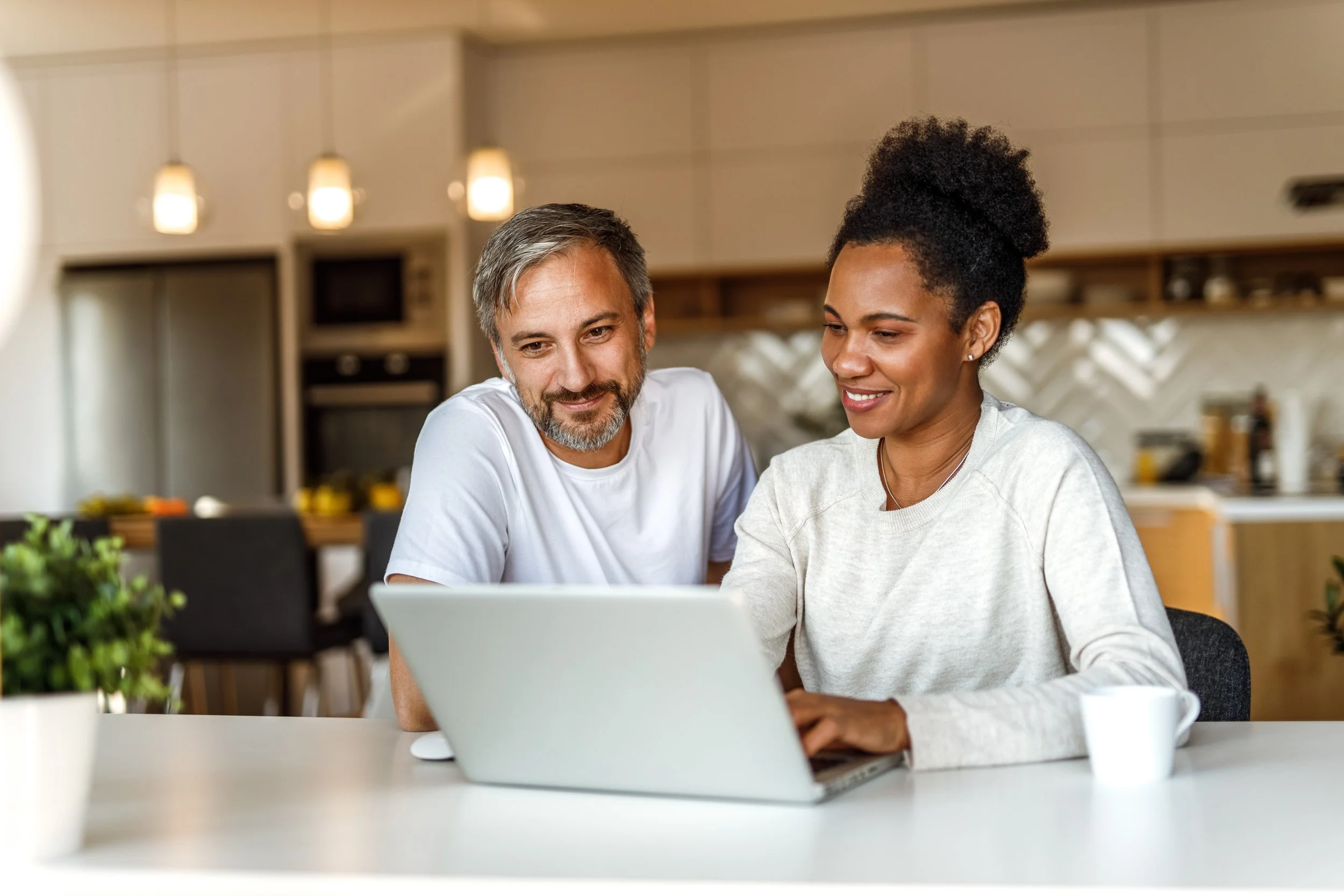 couple-sitting-in-kitchen-with-laptop-smiling-at-screen