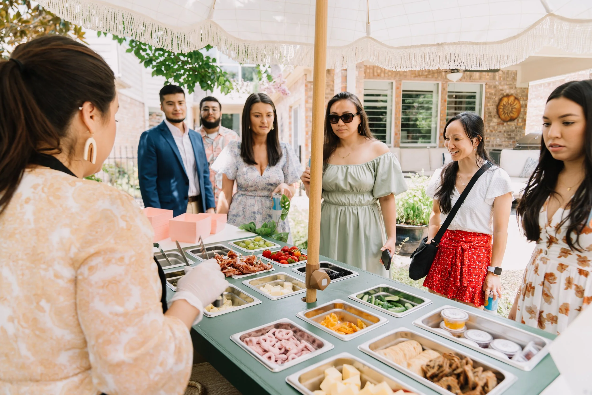 People waiting in line at a food stand with various food items, under a white canopy outdoors