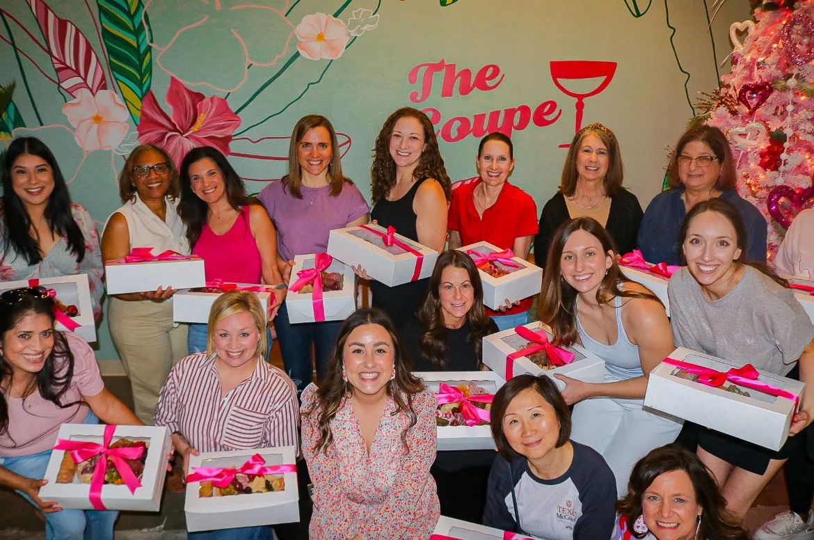 Group of women holding gift boxes with pink ribbons at a party or celebration, decorated with colorful flowers and Christmas tree in the background