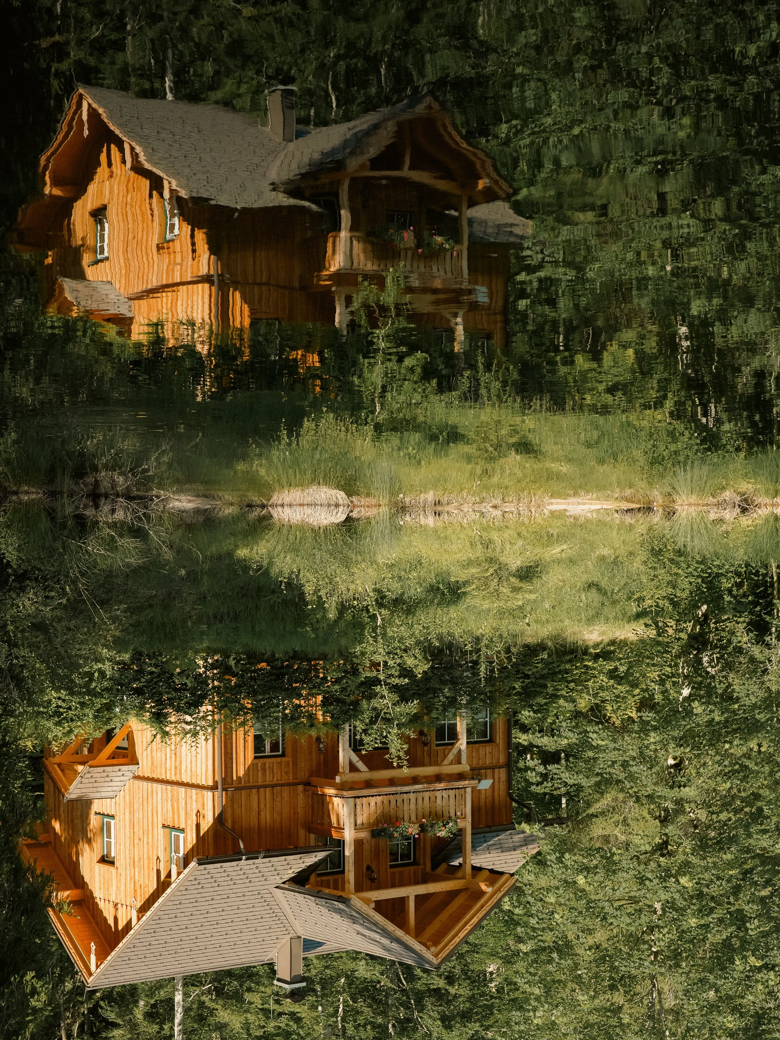 Reflection of a wooden house with a porch in a calm body of water, surrounded by lush greenery.