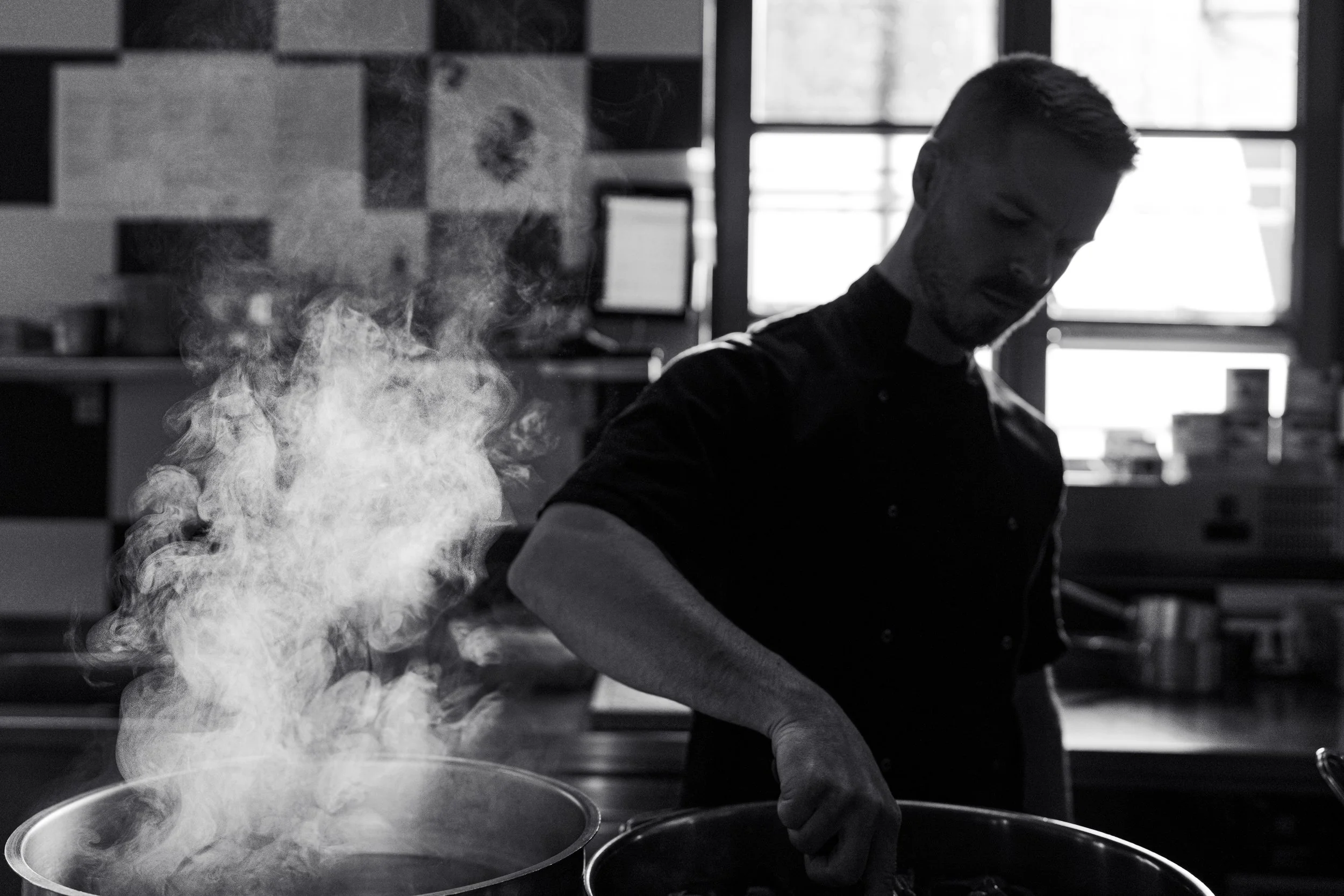 Chef cooking in kitchen with steam rising from pot, monochrome image