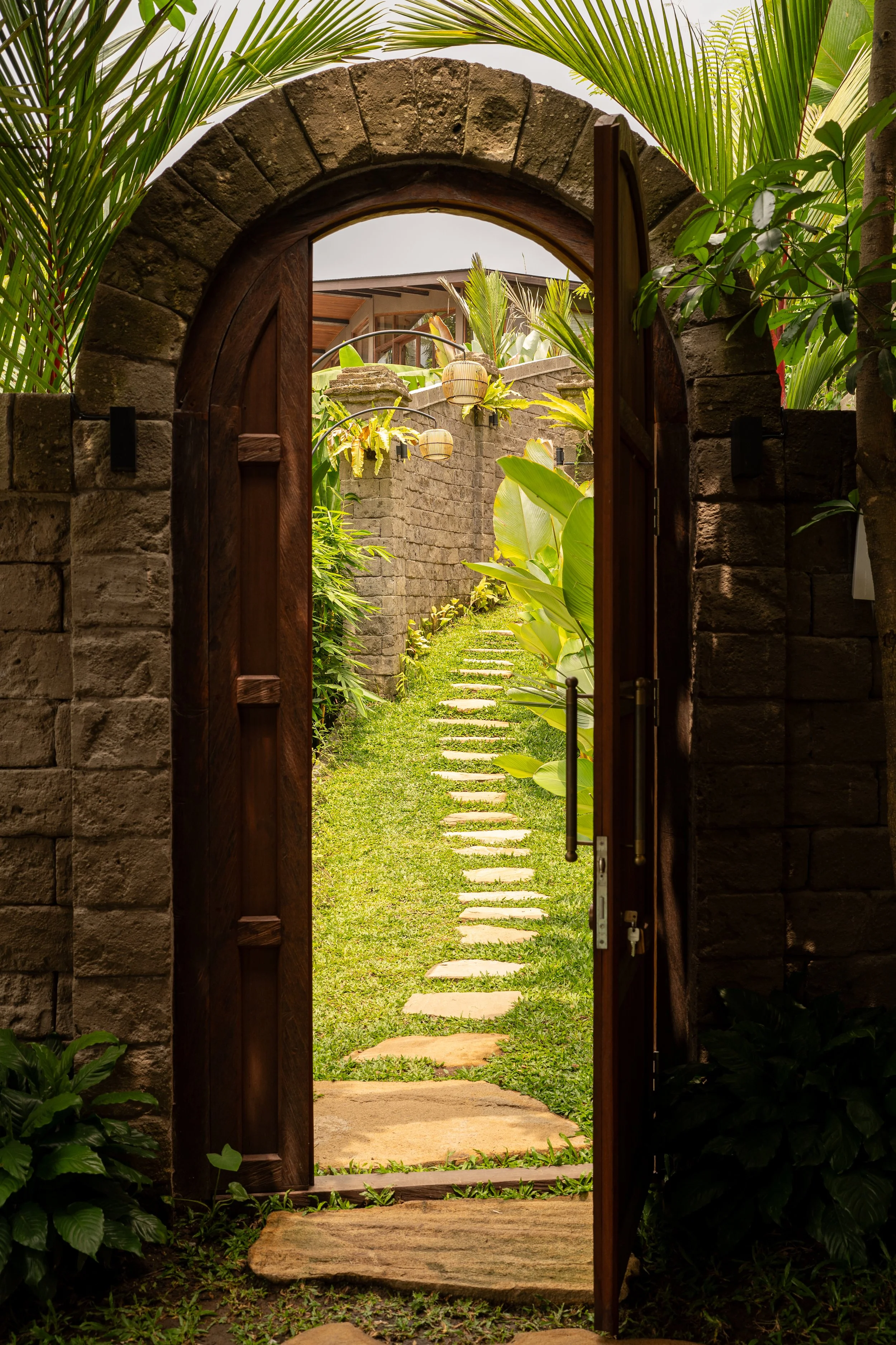 Open wooden gate leading to a stone pathway through a lush garden.