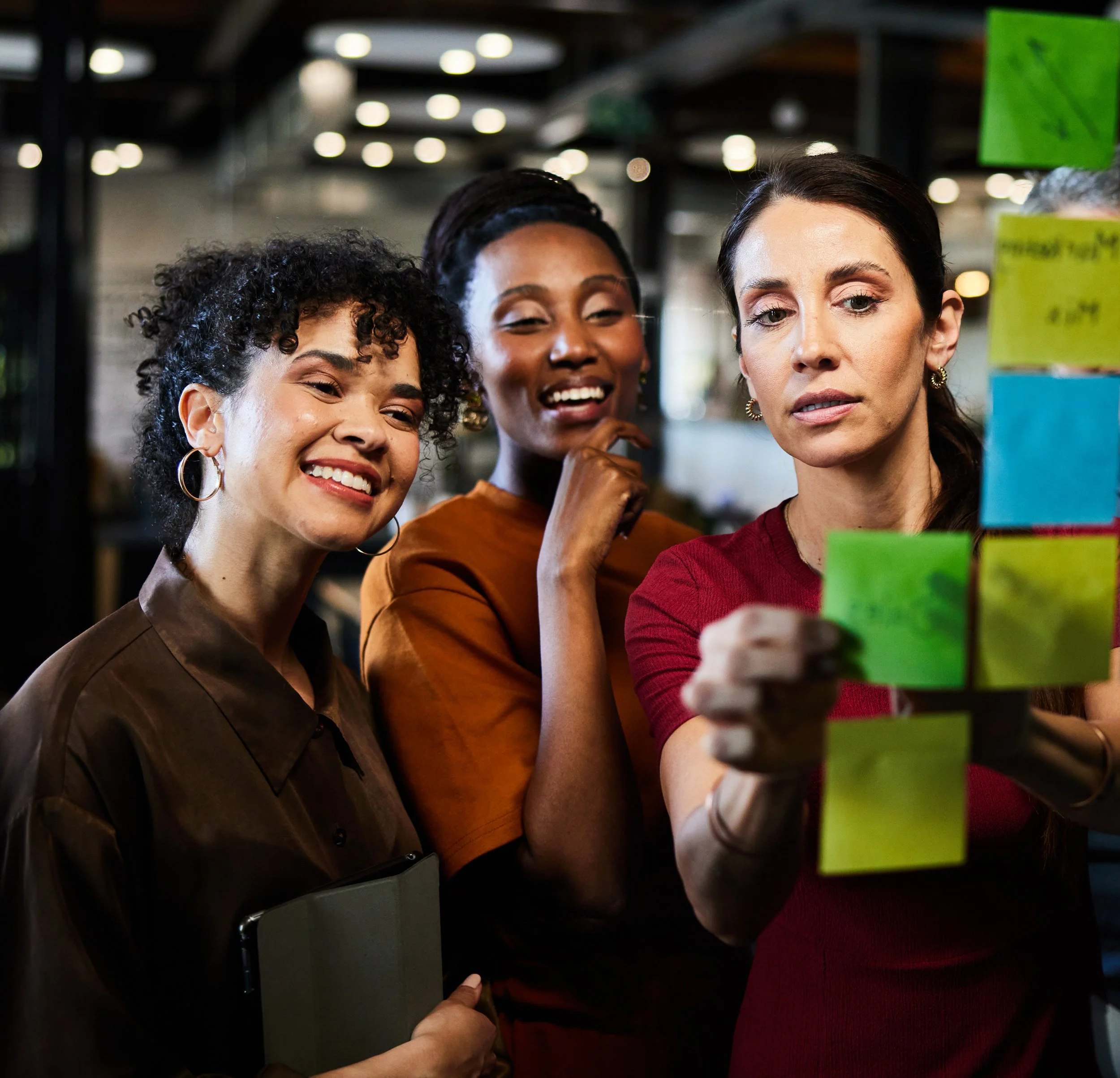 Three coworkers collaborating at a board covered in colorful post-it notes, representing qualitative data analysis, mixed-methods research consulting, and community listening sessions for health and human services.