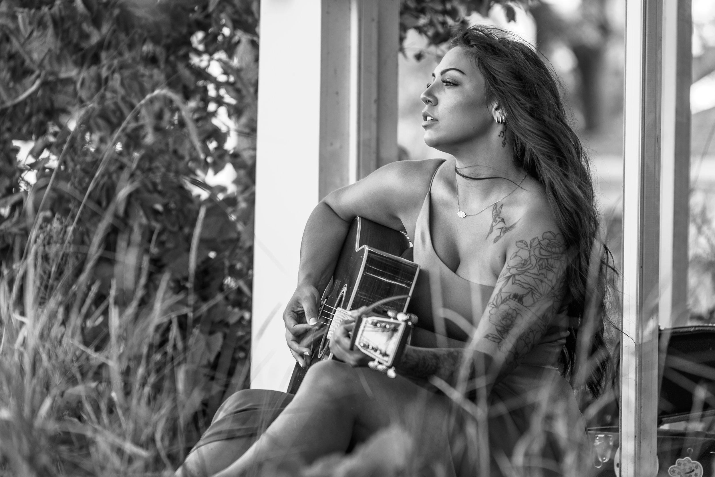 Booking Promo #7. Emily Raff with tattoos playing a guitar outdoors in black and white.