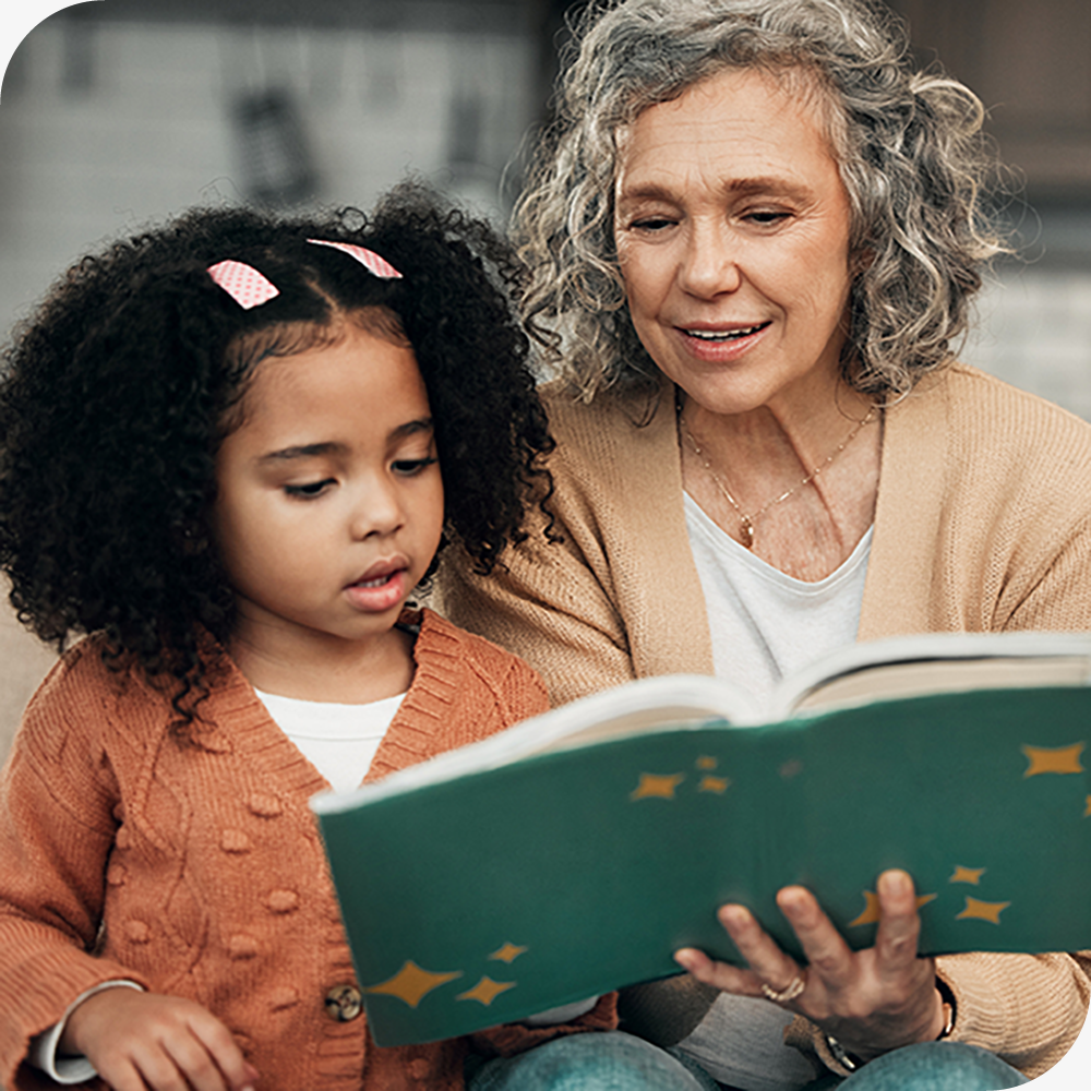 An older woman and young girl reading a book together in a cozy setting.