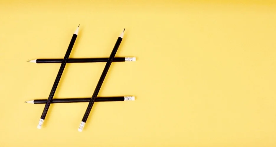 Four black pencils arranged in a hashtag shape on a yellow background representing hashtag social media strategy developed by a social media manager.