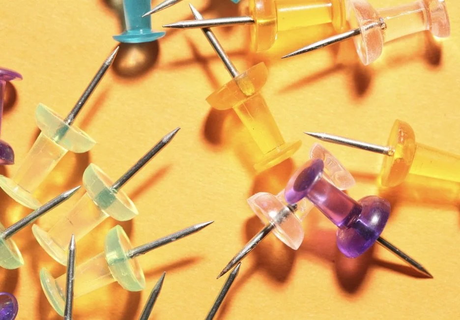 Colorful push pins scattered on an orange surface representing busy business that needs a virtual support specialist