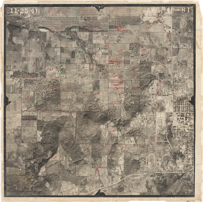 Aerial black-and-white map of a rural area with fields, forests, roads, and a small community, with red handwritten notes and markings.