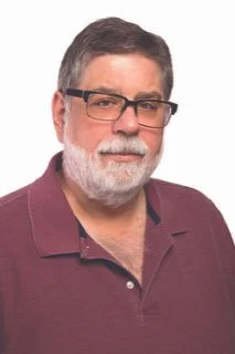 A middle-aged man with gray hair, a beard, and glasses wearing a maroon polo shirt looking at the camera.