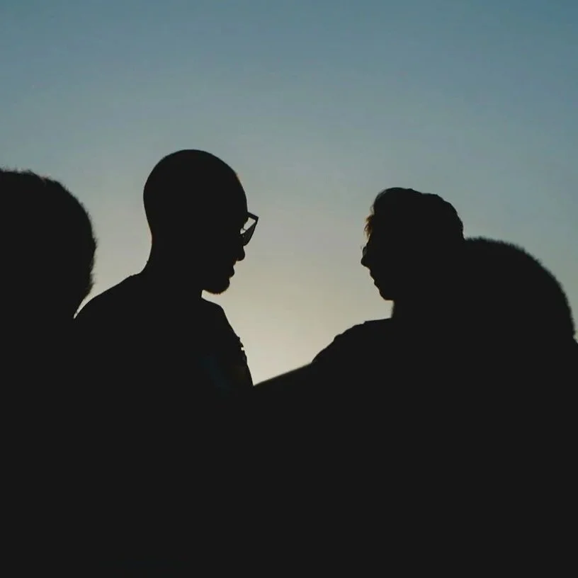 Silhouettes of four people facing each other against a sunset sky.