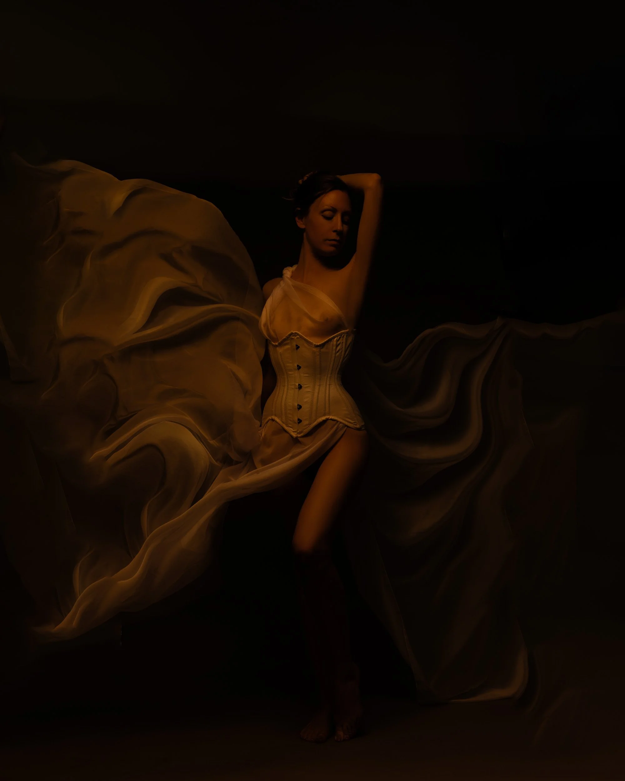 Fine art boudoir portrait by Amanda Chantee near Portland, Oregon, featuring a woman in a light corset framed by flowing golden fabric and dramatic shadow.