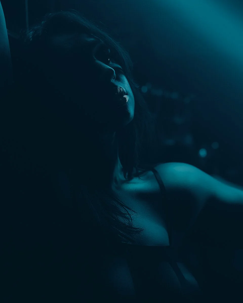 Close-up fine art boudoir portrait by Amanda Chantee featuring a woman under deep teal lighting with dramatic shadow and body contour.