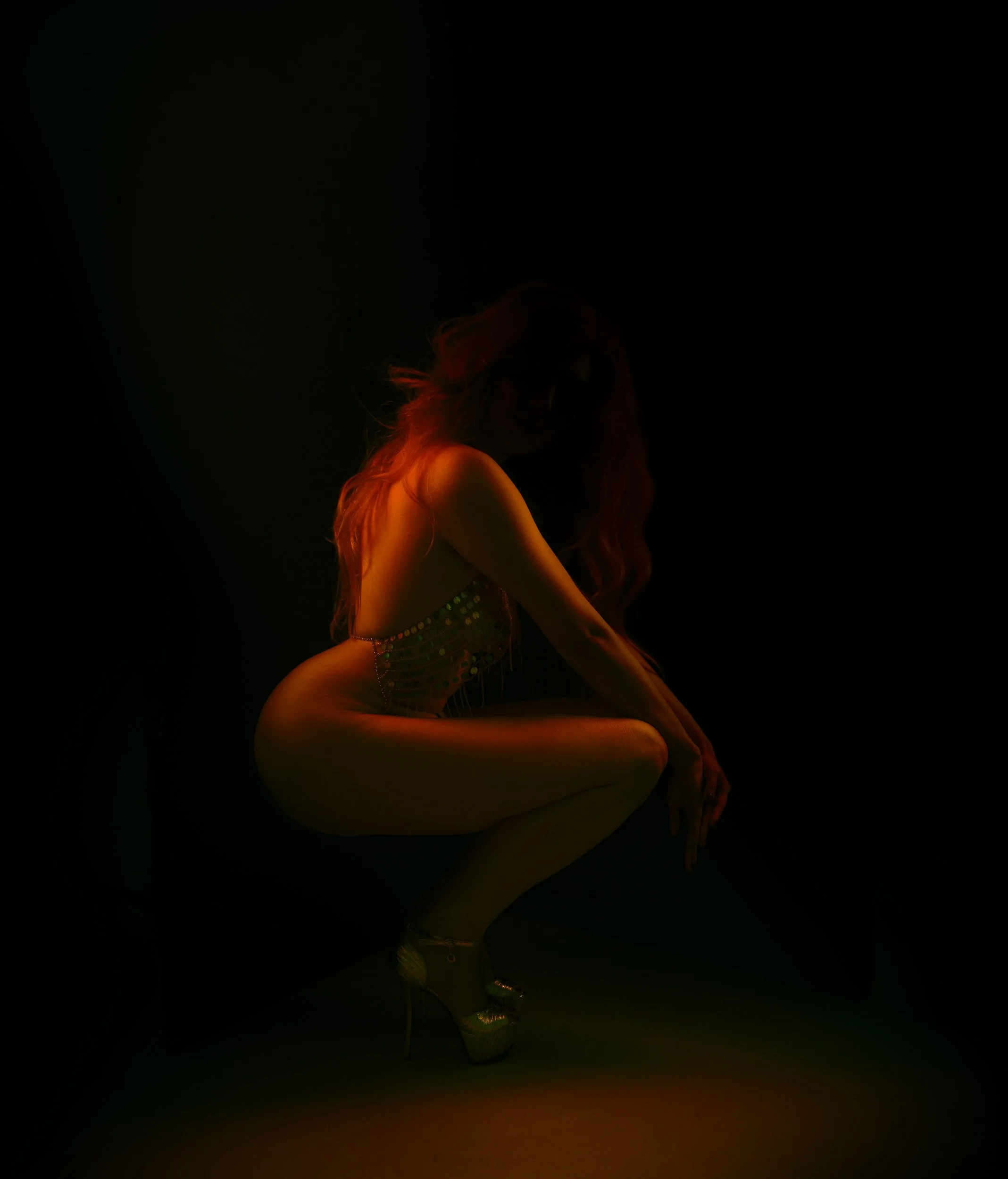 Artistic boudoir portrait by Amanda Chantee of a woman crouched under warm amber lighting with deep shadow and sculptural posing.