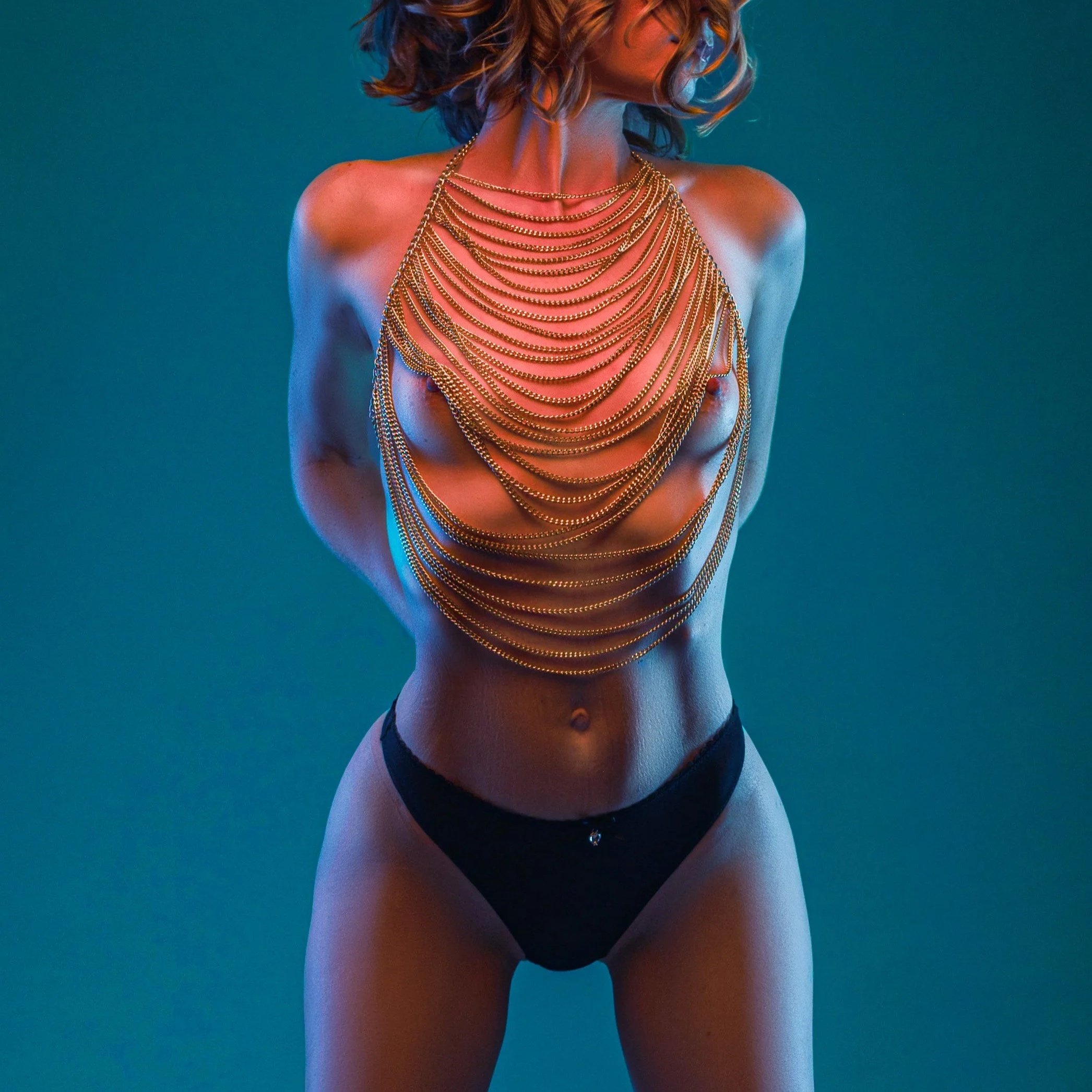 Editorial boudoir portrait by Amanda Chantee featuring a woman in black lingerie and layered body chains under teal and warm studio lighting.