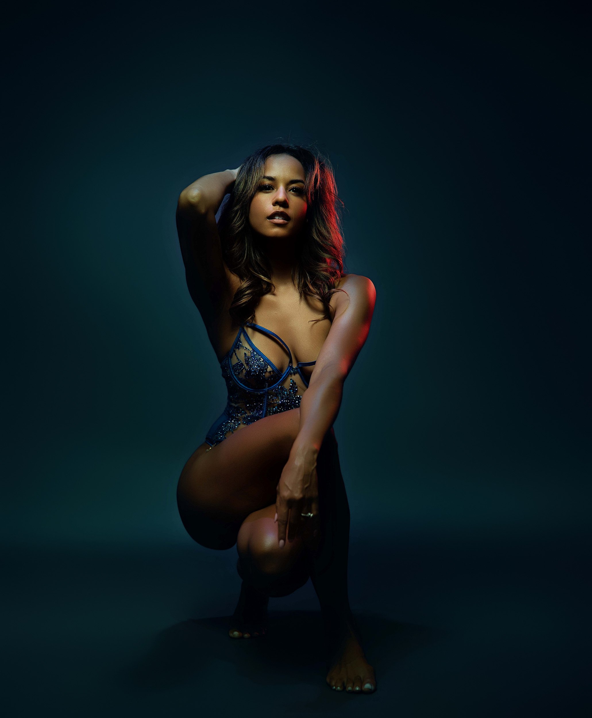 Luxury boudoir portrait by Amanda Chantee featuring a woman in blue lingerie posing under teal and red studio lighting.