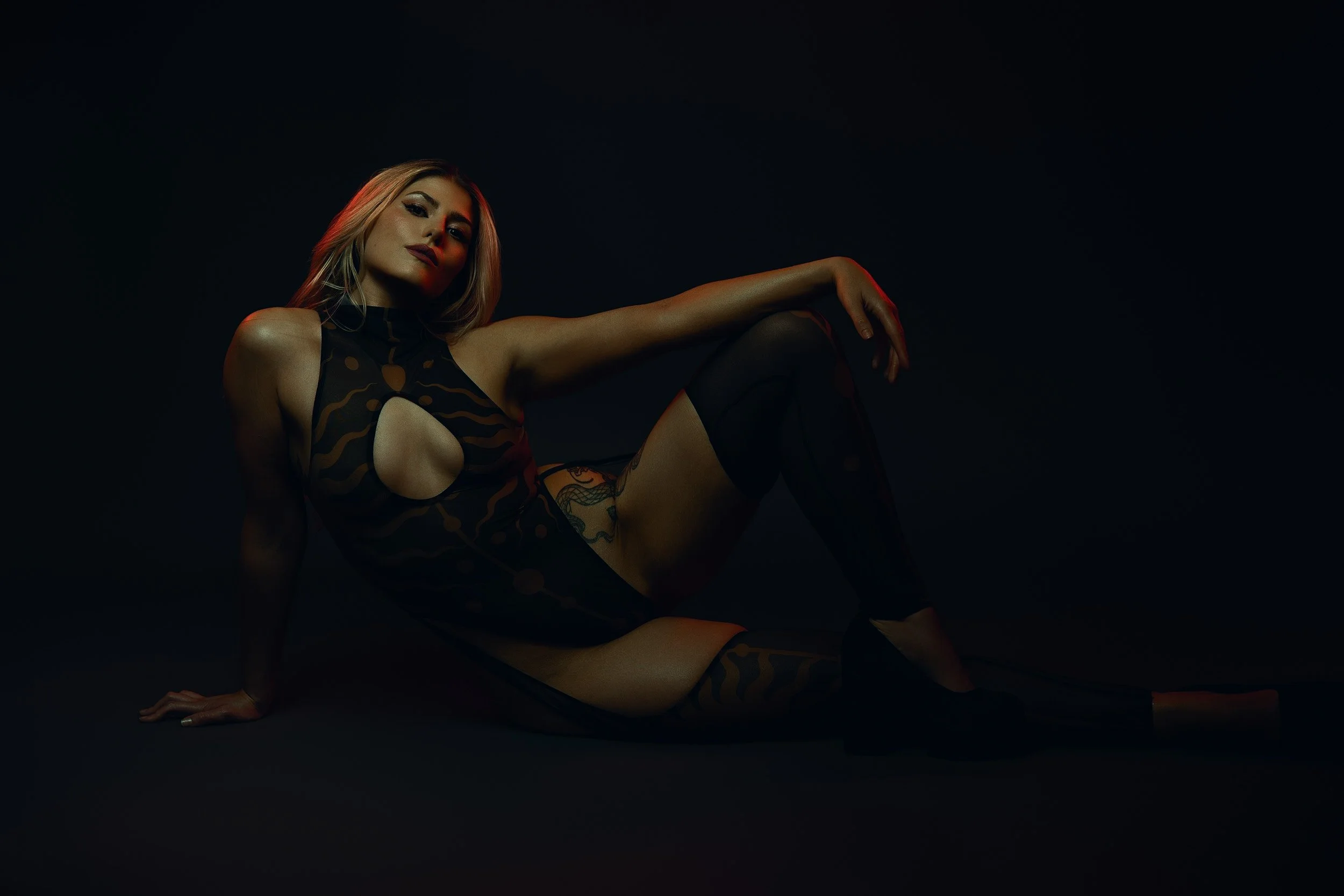 Woman posing on the floor in a black cutout bodysuit and thigh-high stockings during a moody fine art boudoir photography session in Vancouver, Washington.