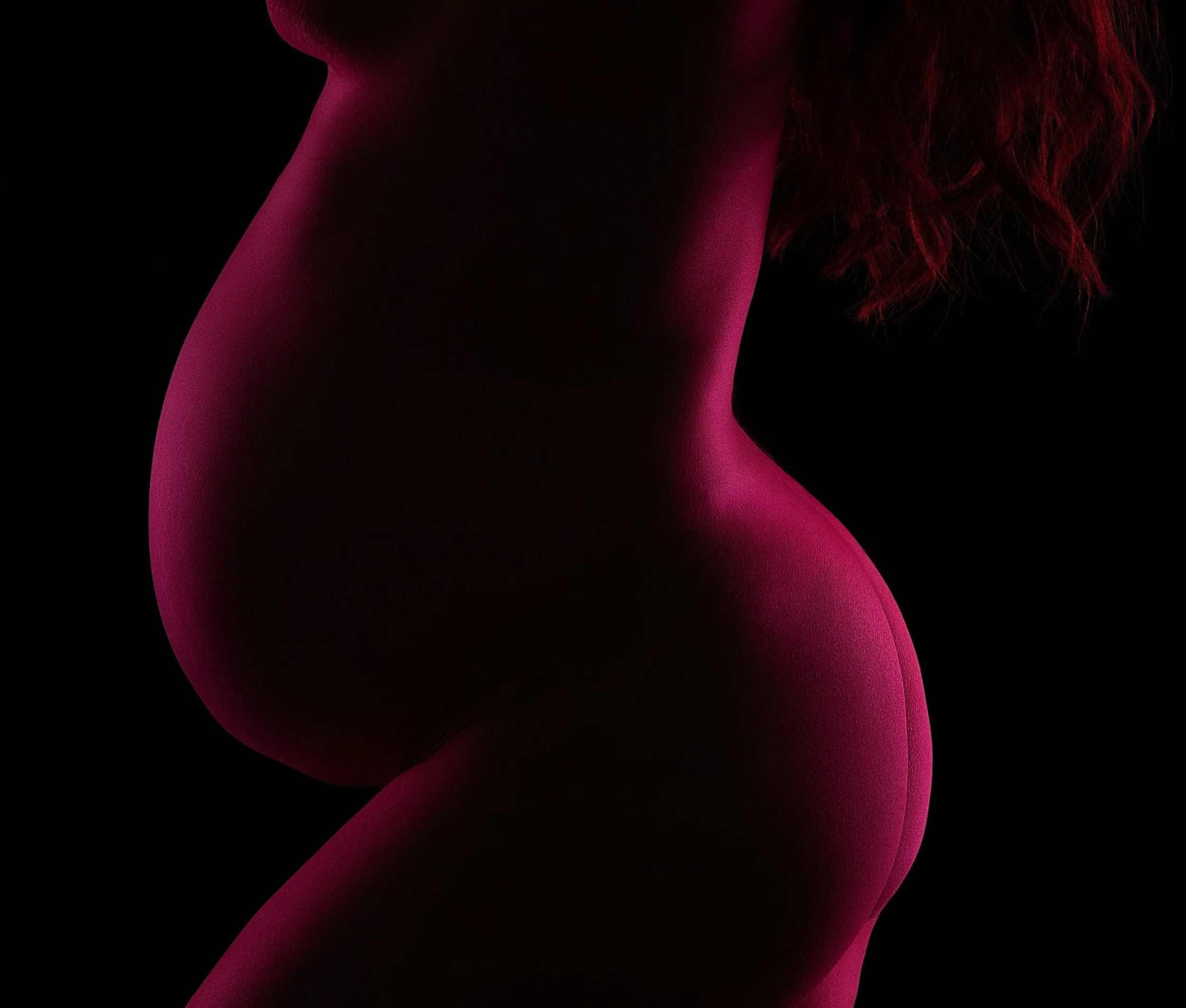 Fine art maternity silhouette in Vancouver, WA, highlighting the curves of pregnancy with vivid magenta rim lighting and deep shadow.