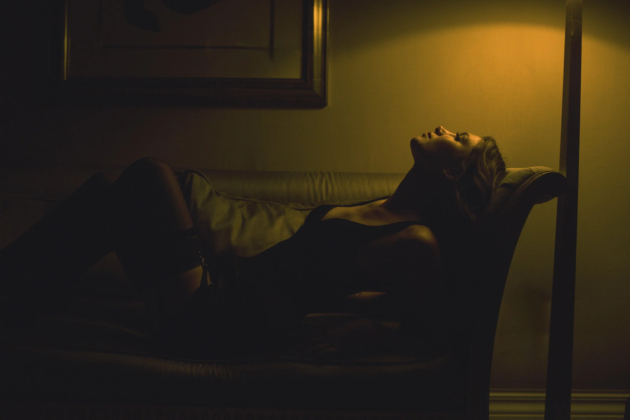 Moody hotel boudoir portrait of a woman reclining on a sofa under warm golden ambient light at the Nines Hotel in Portland, Oregon by Amanda Chantee. 